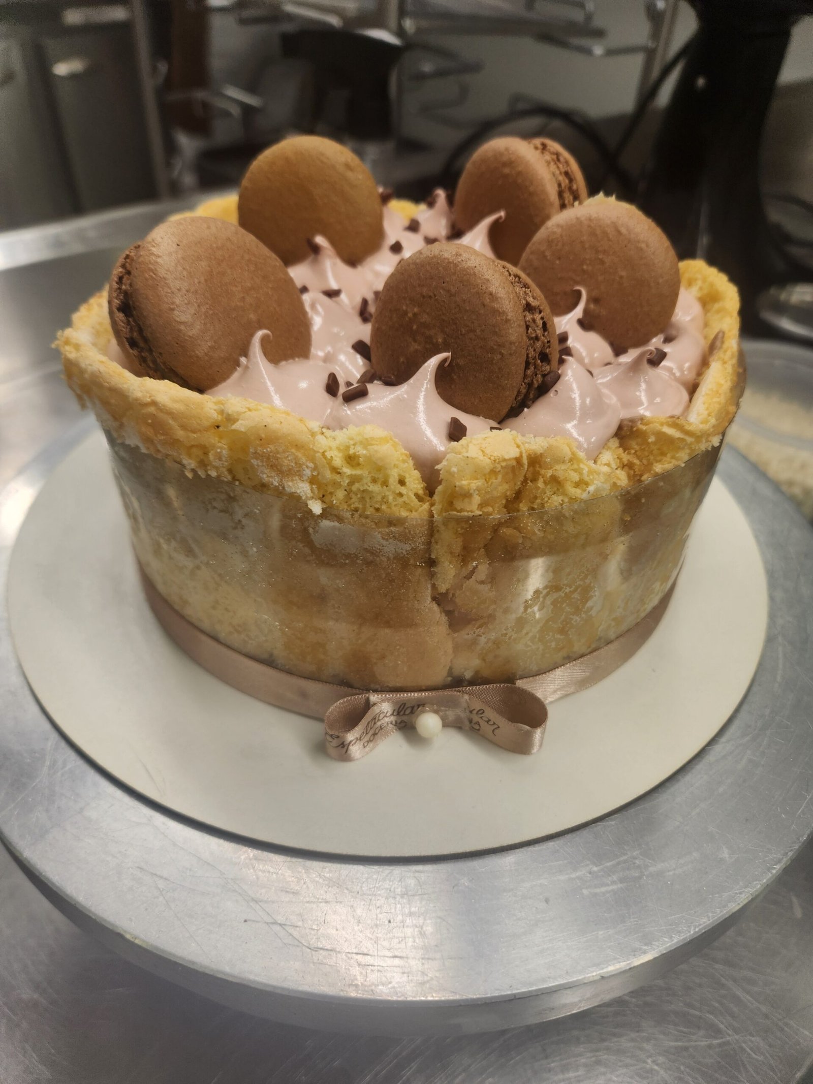 entremet desenformado com a lateral de biscuit intacta, mousse e macarons decorando o topo