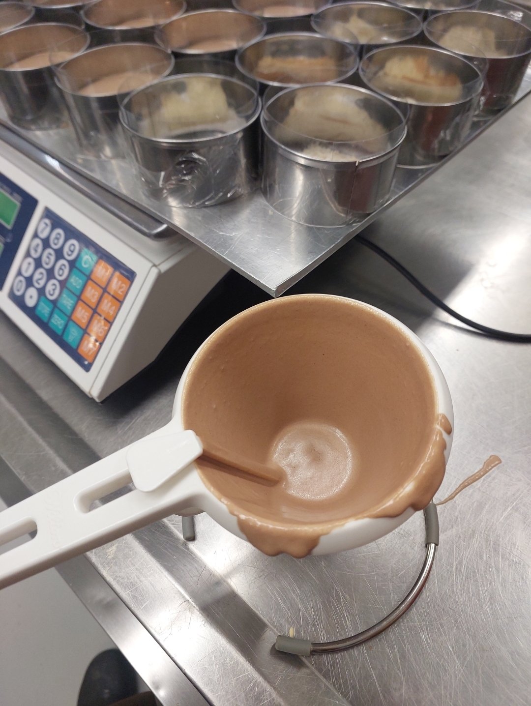 creme aerado fluido em jarra com espátula, aros/copos já preparados ao lado (substituto aproximado: mousse pronta para dosar, mostra a fluidez da mistura na janela de trabalho)