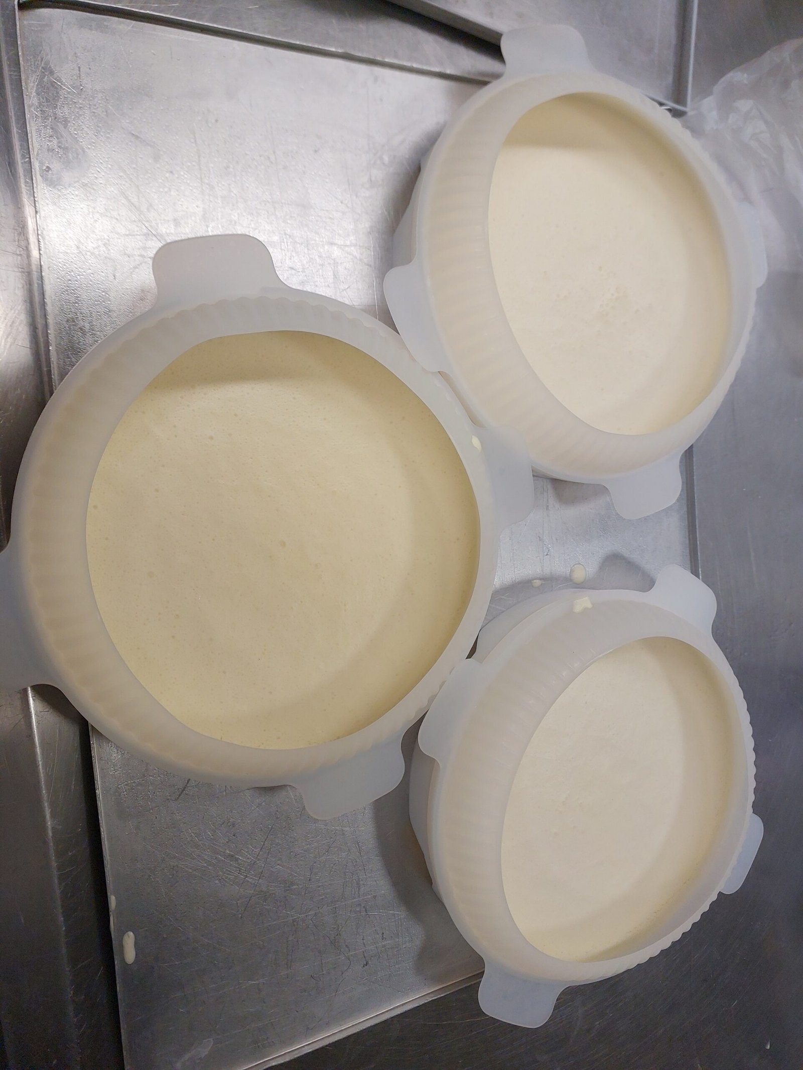três formas de silicone preenchidas com creme aerado claro, superfície lisa, sobre assadeira de inox (substituto aproximado: camada de entremet, não bavaroise identificada — mesmo estágio de mistura vertida antes do frio)