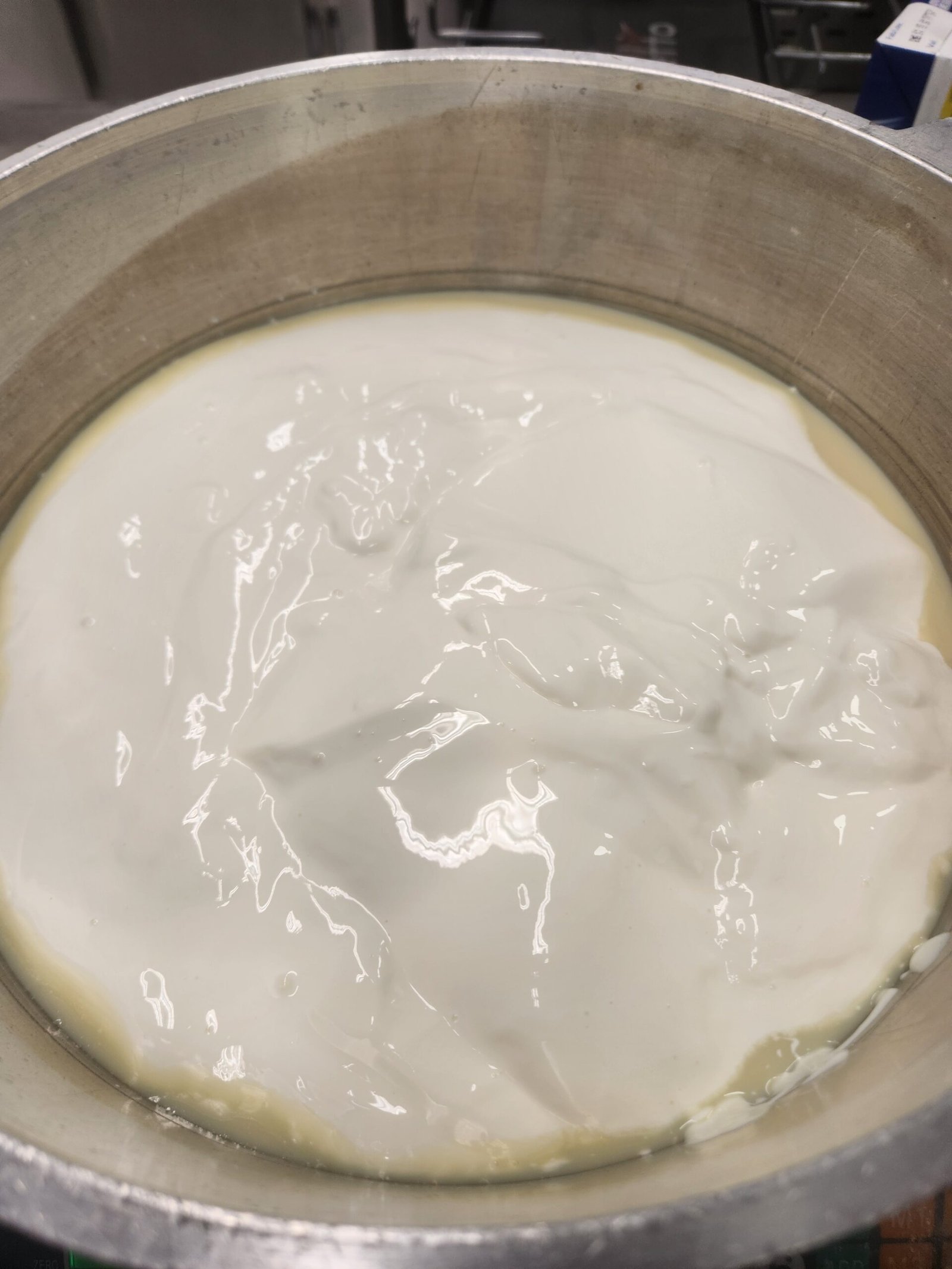 massa láctica branca já espessa e brilhante ocupando a panela larga, com relevo que segura a marca do movimento (substituto aproximado: brigadeiro branco em ponto, não doce de leite — mesmo mecanismo de concentração por evaporação)