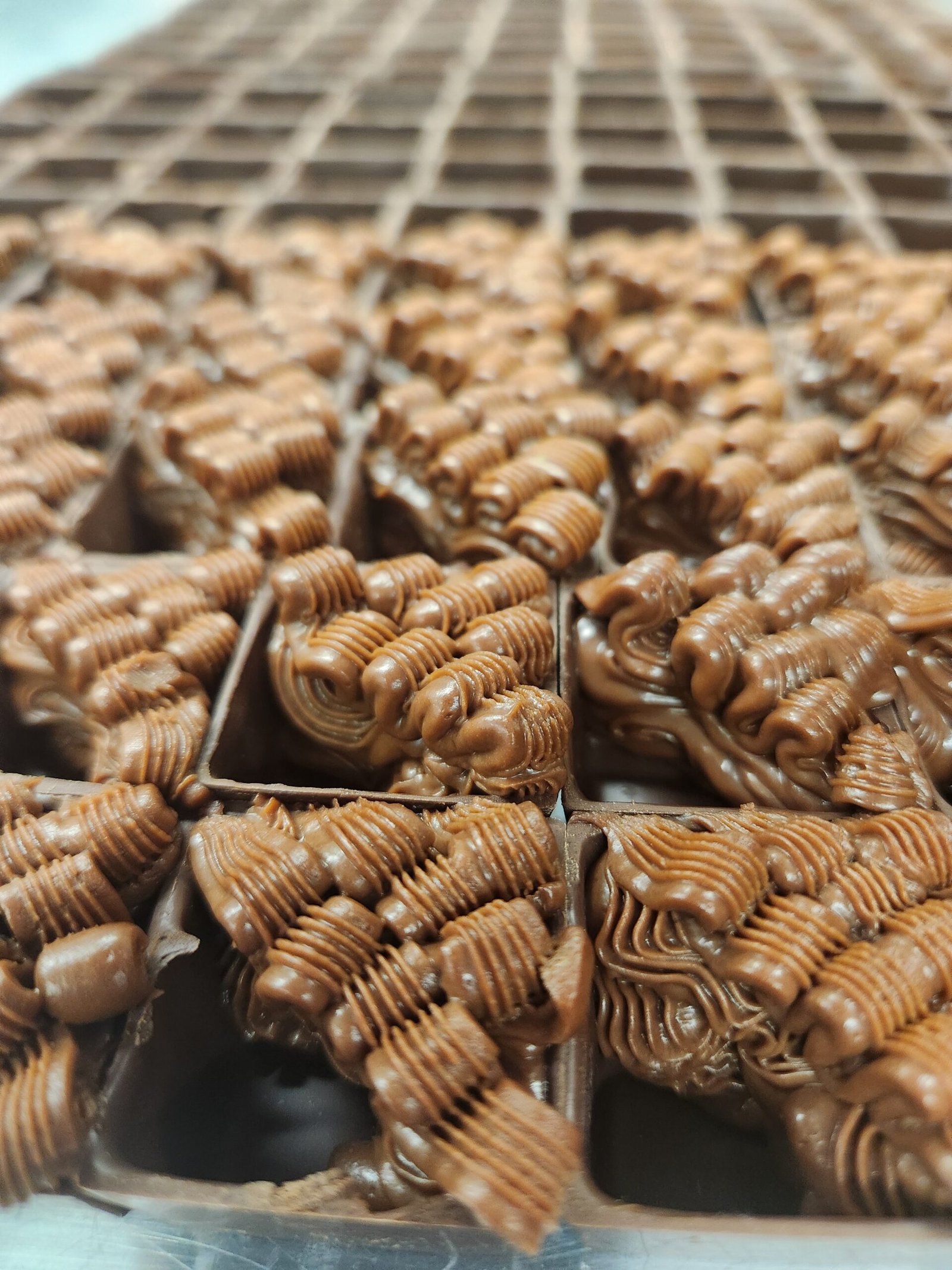 cascas de bombom preenchidas com recheio de chocolate pipado em cordões, textura firme que mantém o desenho do bico (substituto aproximado: recheio de chocolate com creme, não de água)