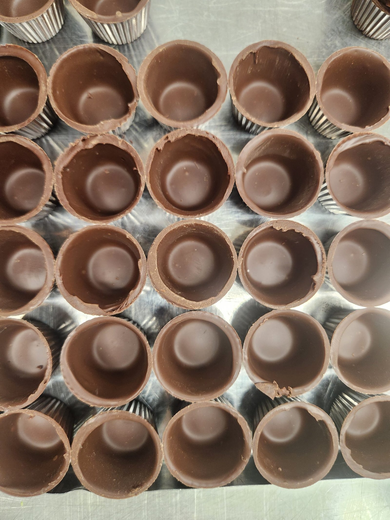 dezenas de cascas redondas de chocolate desmoldadas e alinhadas em bandeja de inox, vazias, prontas para recheio