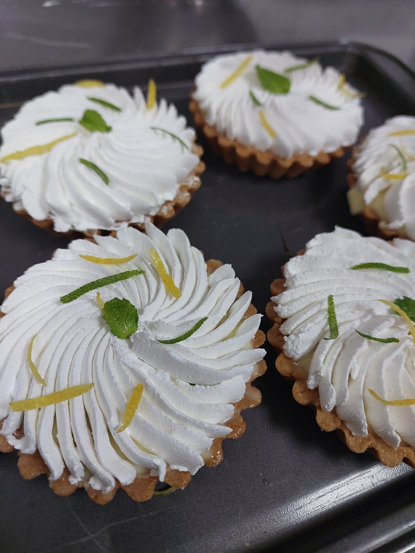 tarteletes de limão finalizadas com chantilly e raspas, com a borda canelada da massa ainda definida em volta do recheio