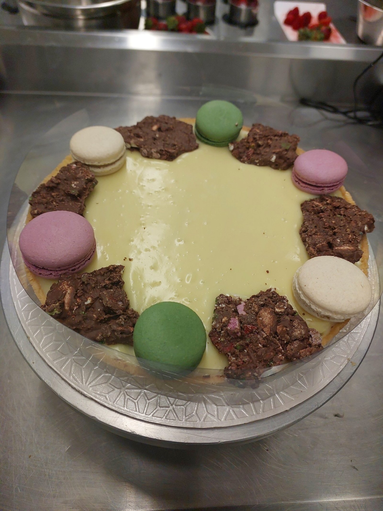 tarte grande com recheio liso à base de chocolate branco e acabamento de crocante e macarons, borda de massa aparecendo em volta
