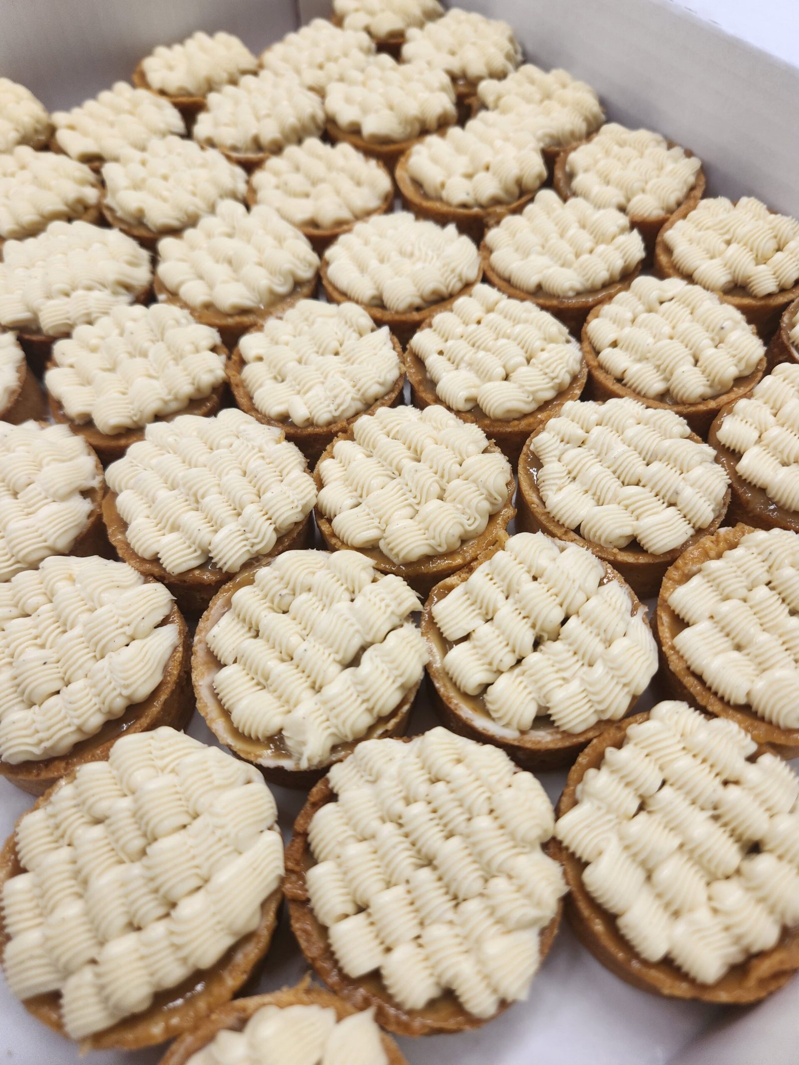dezenas de tarteletes da mesma leva já desenformadas e finalizadas, bordas visíveis lado a lado para comparação de altura (substituto aproximado: peça finalizada em `Doces\Tartes`, não o momento do forno)