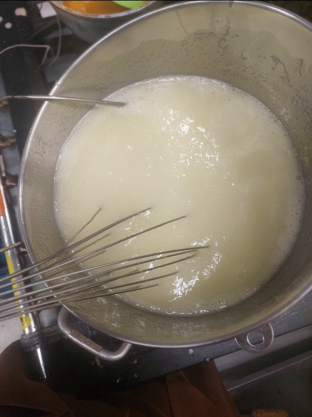 tigela de inox sobre o fogo com claras e açúcar ainda líquidos e leitosos, batedor de arame apoiado