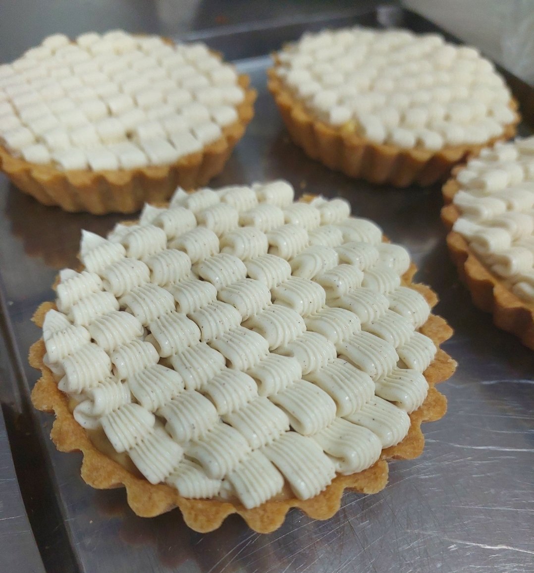 tartes finalizadas em bandeja, cobertura pipada em faixas sobre a base assada, borda de massa nítida em cada peça