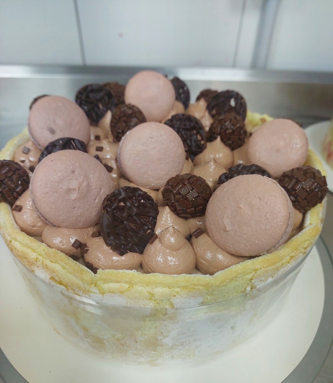 peça cilíndrica desenformada e autoportante: parede de biscuit contínua fechando toda a volta, recheio pipetado até a borda e acabamento de macarons e brigadeiros no topo