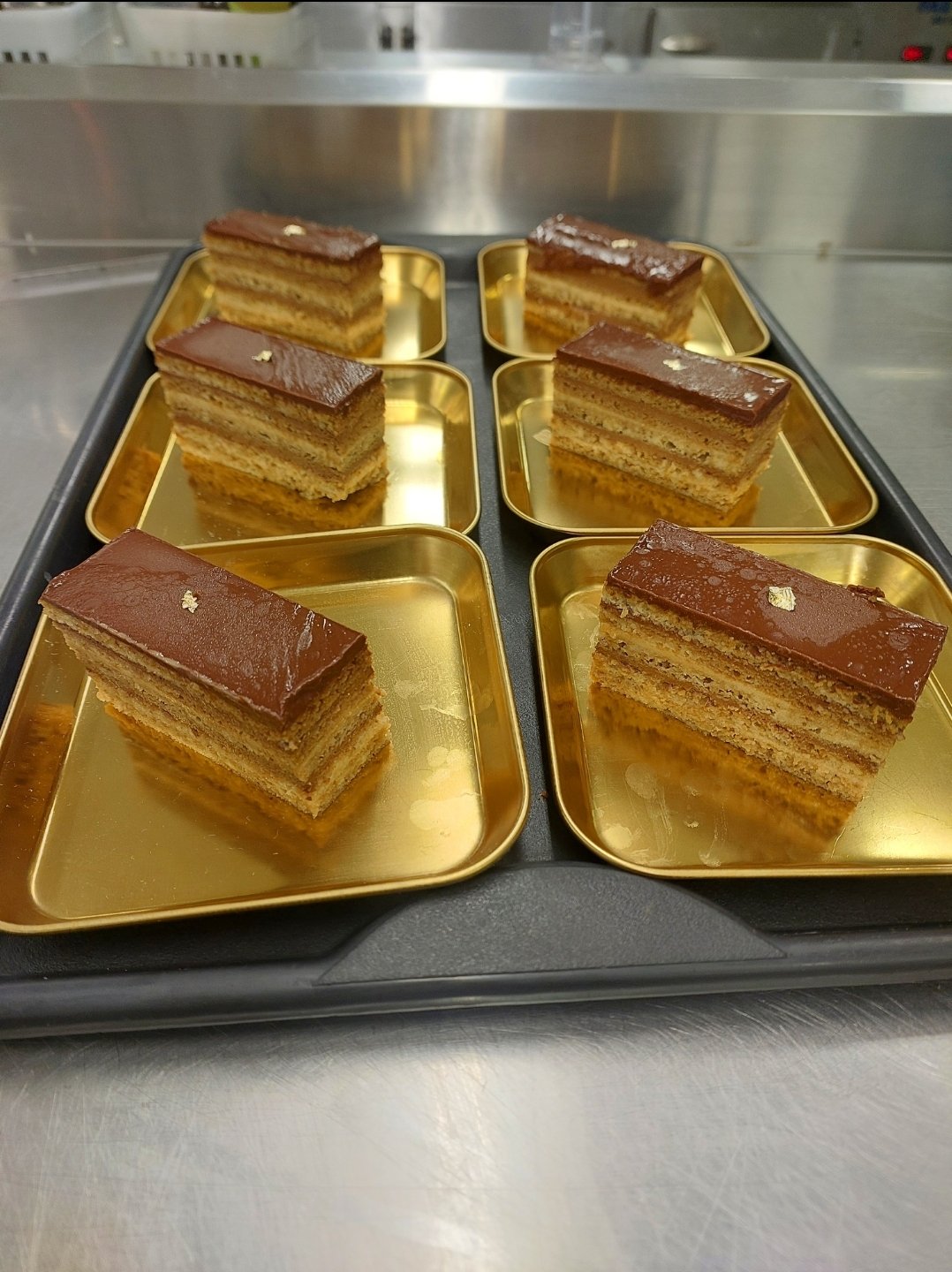 porções em camadas vistas de lado, massa embebida em café alternada com creme, base seca (substituto aproximado: Opéra, massa joconde embebida em café, não savoiardi — mesmo mecanismo de base absorvente entre camadas de creme)