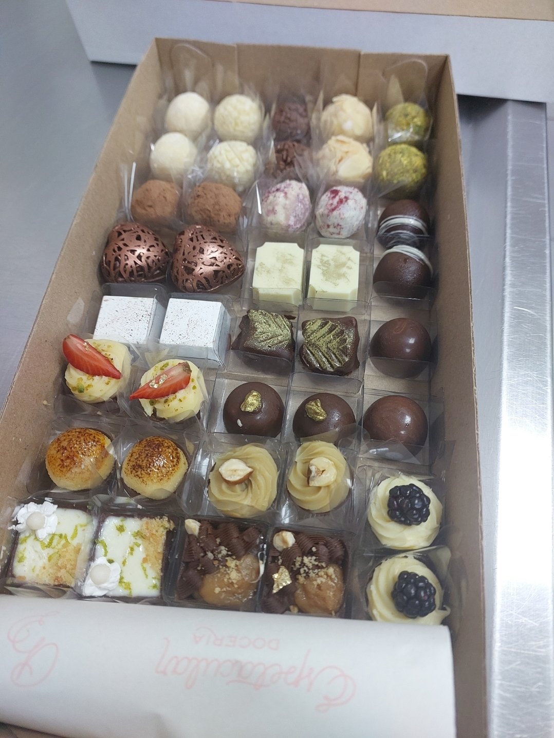 Peças de famílias diferentes na mesma caixa: cascas ao leite, chocolate branco, trufas polvilhadas com cacau e acabamento dourado.