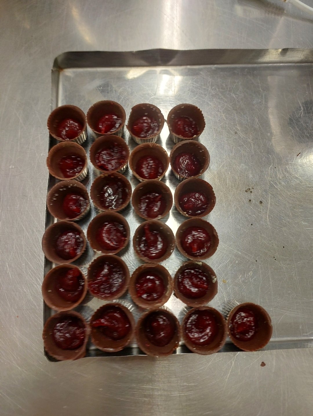 bandeja de inox com cascas redondas de chocolate ao leite preenchidas com recheio vermelho de fruta, vistas de cima