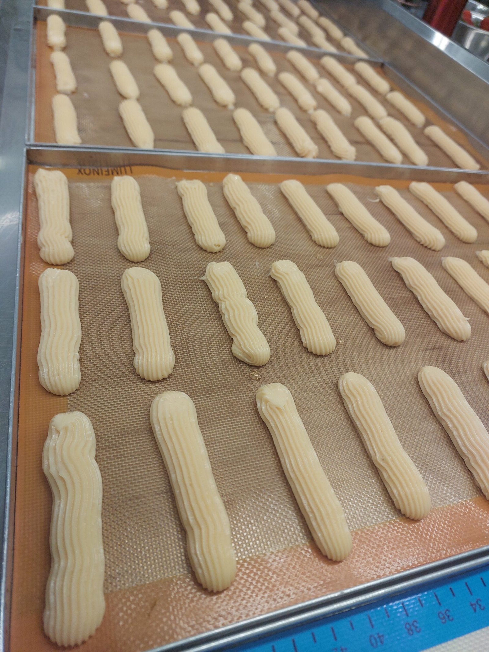 Éclairs crus já pipados, com as ranhuras do bico marcadas e o comprimento uniforme.